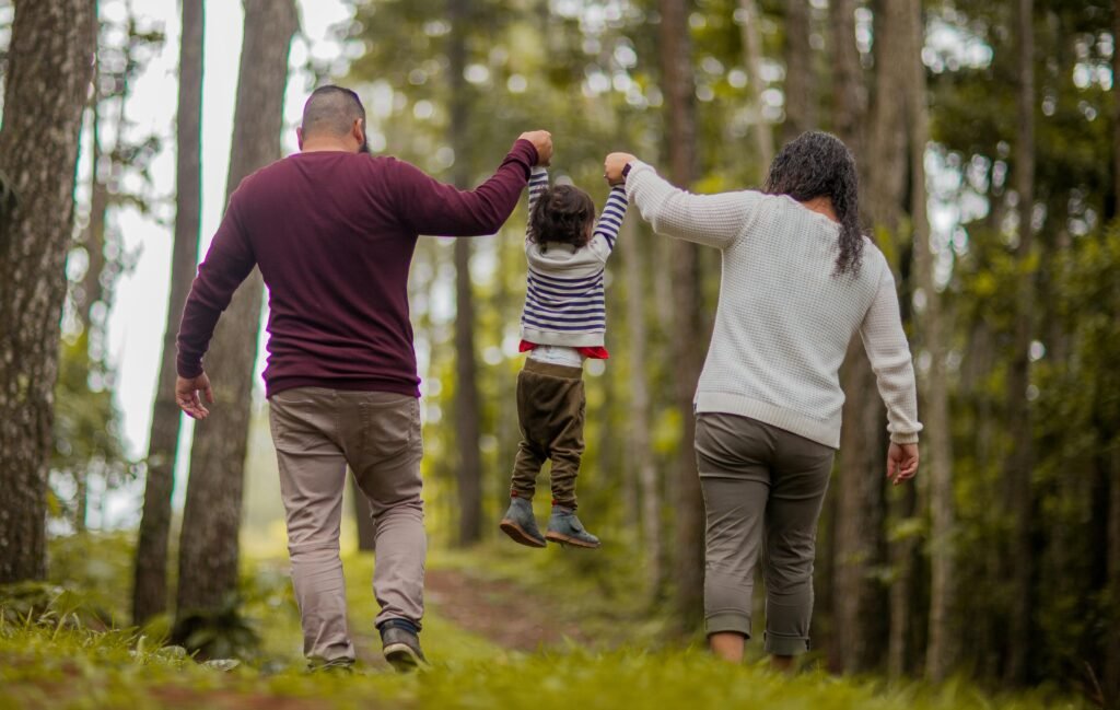 Kreu A happy family walking through a forest, lifting their child playfully outdoors.
