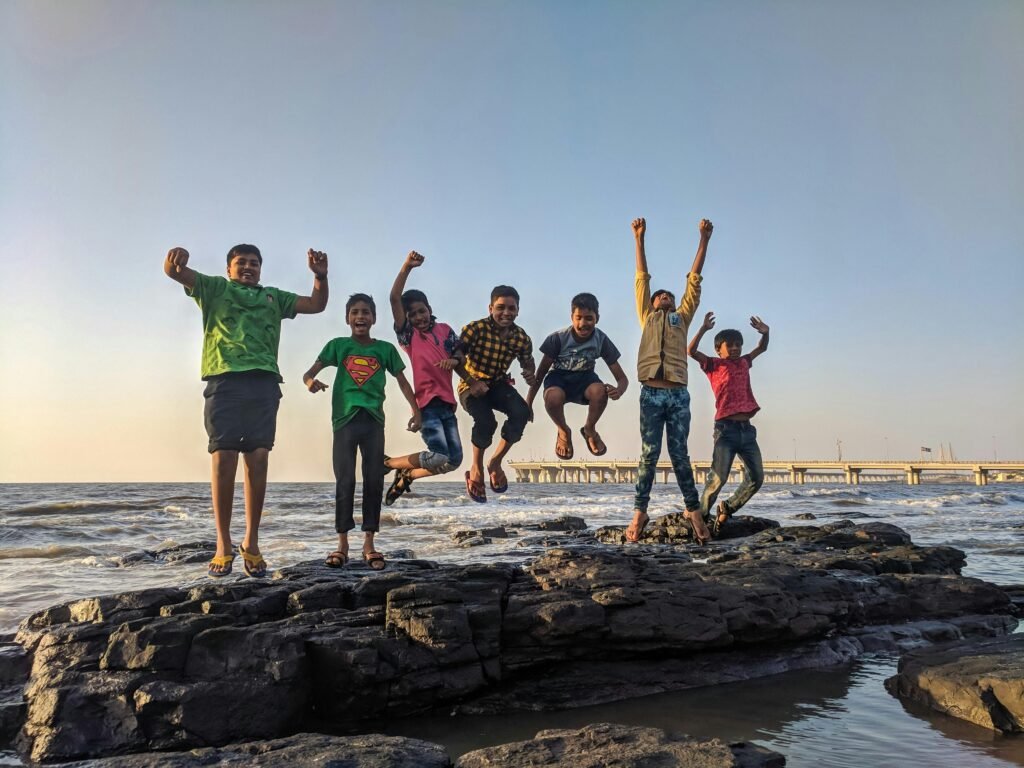 Kreu Group of kids joyfully jumping on rocks by the seaside. Fun and playful moment captured outdoors.